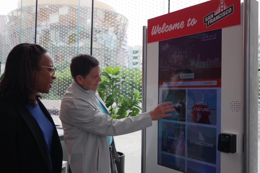 a visitor information center employee showing an attendee how to use the itinerary building on a kiosk screen