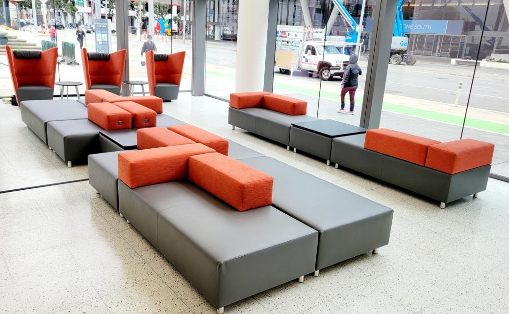 grey & orange lounge furniture in a bright area of the lobby with windows viewing the sidewalk